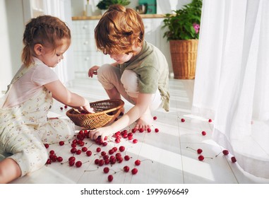 Cute Redhead Kids, Siblings Helping Each Other To Collect Cherries Scattered On The Floor At The Kitchen At Sunny Summer Day