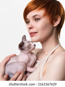 Cute Redhead Young Woman Gently Hugging Sleeping Kitten To Her Chest And Looking Away. Portrait Of Pretty Woman With Short Hair 25 Years Old. Studio Shot On White Background. Part Of Series.