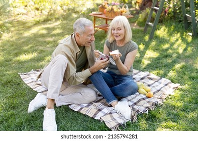 Cute Retired Couple Having Picnic In Their Garden, Sitting On Blanket And Eating Toasts With Jam, Spending Time Together Outdoors And Enjoying Warm Spring Day