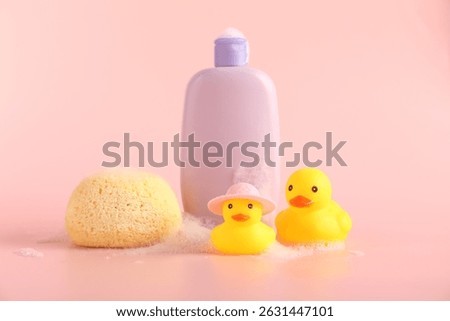 Cute rubber ducks, sponge and bottle of shampoo on pink background
