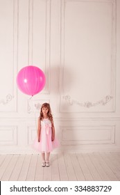 Cute sad girl 4-5 year old holding balloon in room. Looking at camera. Childhood. Alone child. 