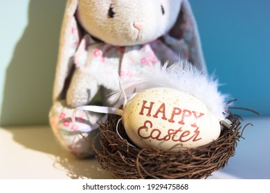 A Cute Sad Toy Bunny On Blue Background And A Nest With An Easter Egg Inside. Egg Hunting Game For Kids.