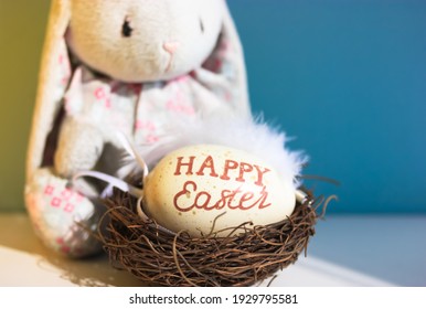 A Cute Sad Toy Bunny On Blue Background And A Nest With An Easter Egg Inside. Egg Hunting Game For Kids.