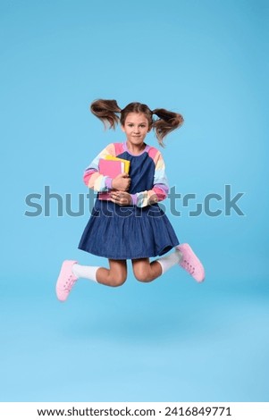 Cute schoolgirl with books jumping on light blue background