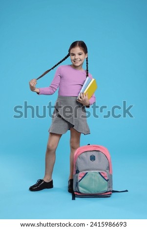Cute schoolgirl with books on light blue background