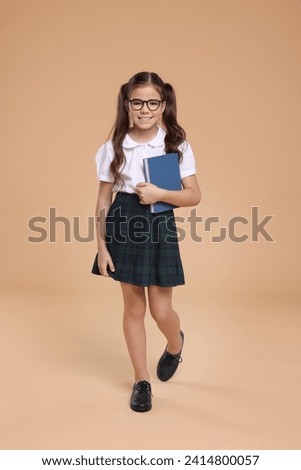 Cute schoolgirl in glasses with book on beige background