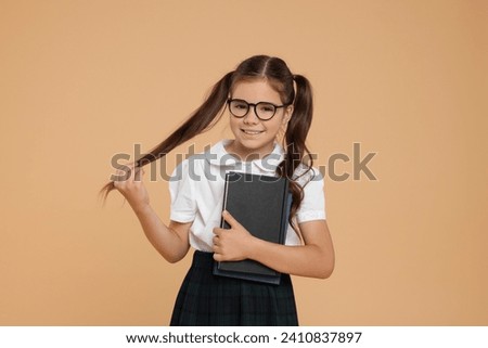 Cute schoolgirl in glasses with books on beige background