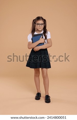 Cute schoolgirl in glasses with books on beige background