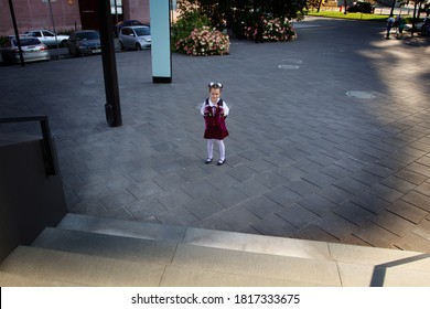 Cute Schoolgirl Wearing Uniform And School Bag Standing On The Empty School Yard, Looking Up. Shot From Above