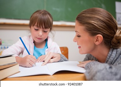 Cute schoolgirl writing while her teacher is talking in classroom