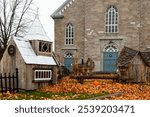 Cute seasonal decorations including a miniature church and other wooden buildings in front of the historic 1858 Saint-Michel stone church, Saint-Michel-de-Bellechasse, Quebec, Canada