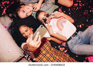 Cute selfies only. High angle view of three happy friends taking a selfie while lying on the floor at a house party. Group of cheerful female friends having fun together on the weekend. - Powered by Shutterstock