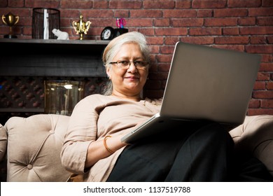 Cute Senior Indian/asian Lady Sitting On Recliners Chair Or Sofa Reading Book Or Using Tab Or Laptop Computer