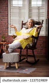 Cute Senior Indian/asian Lady Sitting On Recliners Chair Or Sofa Reading Book Or Using Tab Or Laptop Computer