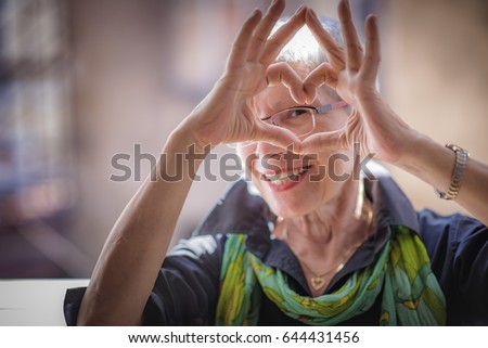 Cute senior old woman making a heart shape with her hands and fingers