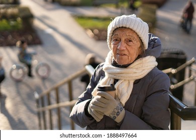 Cute senior woman in city drinks coffee with herself in winter coat and warm hat, scarf and knitted gloves in sunny winter weather. Handsome old female with paper cup of morning coffee to go. - Powered by Shutterstock