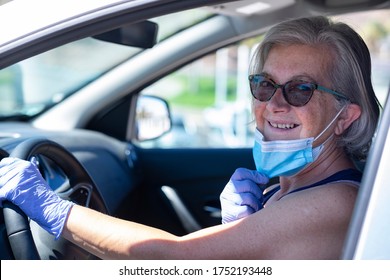 Cute Senior Woman With Sunglasses Driving Silver Car Moves Away From Face Mask Against Coronavirus - New Normal Life Until End Of Pandemic