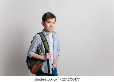 a cute serious cheerful 10 year old teenager school kid boy in glasses, blue shirt and jeans with a backpack showing a finger up isolated on white background. Education concept.