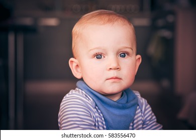 Cute Serious One-year-old Toddler Wearing A Navy Blue Bib And Striped Top - Close Up Portrait Of A Beautiful Sad Emotional Baby Boy With Hurt Feelings And Lovely Wet Eyes - Muted Colors Vintage Effect