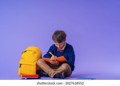 Cute serious schoolboy puts office supplies in a backpack on a purple background. Preparation for school. Back to school. Self-Assembly of a school backpack. - Shutterstock ID 2027618552