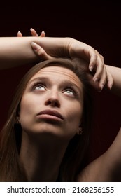 Cute Serious Worried Girl Against Dark Red Background. Brunette Lady Close Up Portrait Looking Up Holding Hands Up 