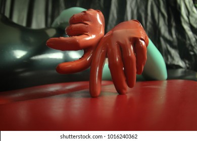 cute short-haired blonde girl posing in latex catsuit and rubber red gloves, alone on a dark background