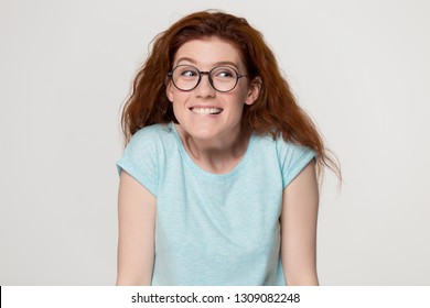 Cute Shy Awkward Redhead Teen Girl In Glasses Biting Lips Feeling Embarrassed, Funny Young Red-haired Woman Student Confused Nervous Before Exam Isolated On White Grey Blank Studio Background