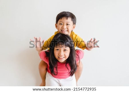 Cute Sibling sister and brother asian Korean Thai portrait kids.Asian children boy child siblings riding the back his sister on white wall at home.fun family.homeschool kid brother sister.hormones kid