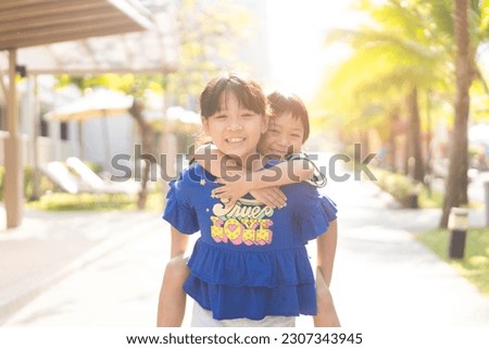 Cute Sibling sister and brother asian Korean Thai portrait kids.Asian children boy child siblings riding the back his sister on the outdoor park.fun family.homeschool kid brother sister.helper sister.