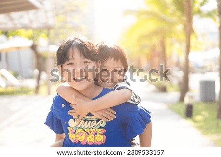 Cute Sibling sister and brother asian Korean Thai portrait kids.Asian children boy child siblings riding the back his sister on the outdoor park.fun family.homeschool kid brother sister.helper sister.