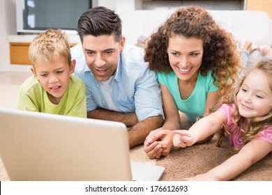 Cute siblings lying on the rug using laptop with their parents at home in living room - Powered by Shutterstock