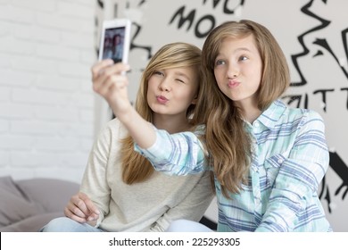 Cute sisters pouting while taking photos with smart phone at home