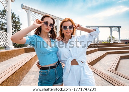 Cute sisters in trendy sunglasses walk in the summer in the park on a sunny day.