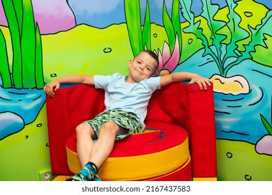 A Cute Six Year Old Boy Sits On A Colorful Soft Throne In A Play Center For Kids