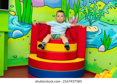 A Cute Six Year Old Boy Sits On A Colorful Soft Throne In A Play Center For Kids