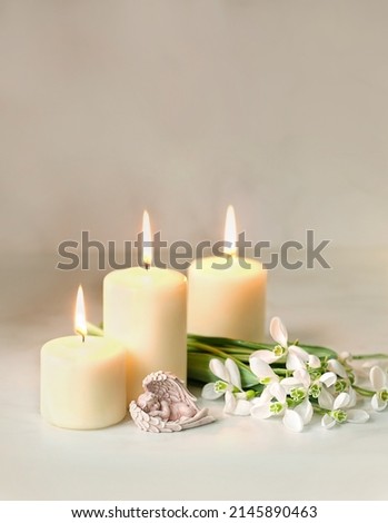 Cute sleeping angel, snowdrops flowers and candles on table, blurred abstract background. Religious church holiday. symbol of faith in God, Christianity Feast. Romantic relaxation composition