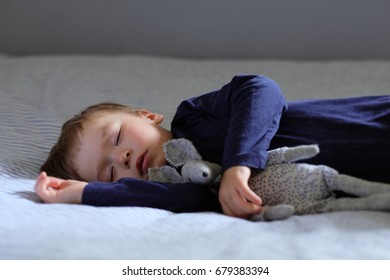 Cute sleeping baby with teddy bear on the bed. Portrait with a copy space.