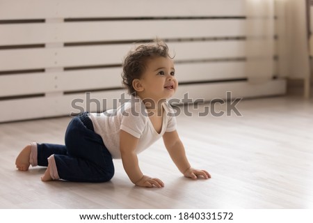 Cute small african American toddler baby child crawl on warm wooden home floor. Smiling little biracial infant kid play in children room indoors, explore world. Childcare, upbringing concept.