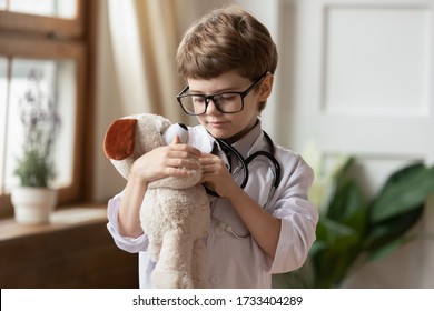 Cute small boy child in white medical uniform examine listen to teddy bear heartbeat with stethoscope, caring little kid act as doctor do checkup of plush toy in hospital, healthcare concept