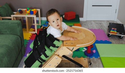 Cute small boy with coordination disorders uses supportive equipment to assist with physical rehabilitation while playing in a vibrant therapy space