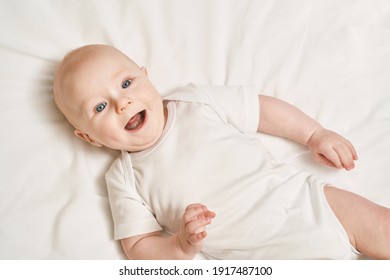 Cute Small Boy Lying At Bed. Childhood Concept. Light Background. Smiling Child. Happy Emotion. Copyspace. Stay Home. Onesie Mockup. White Clothes