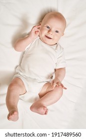 Cute small boy lying at bed. Childhood concept. Light background. Smiling child. Happy emotion. Copyspace. Stay home. Onesie mockup. White clothes. Full body
