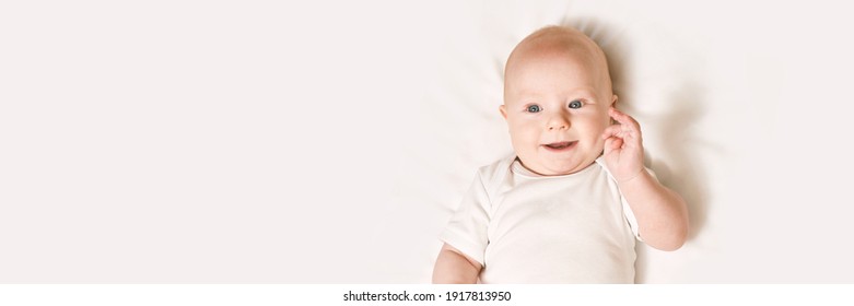 Cute small boy lying at bed. Childhood concept. Light background. Smiling child. Happy emotion. Copyspace. Stay home. Mockup. Horizontal banner. White clothes
