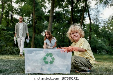 Cute small boy sitting near recycle bin and smiling at camera while collecting plastic waste in forest or park with young happy parents eco activists. Environmental conservation and ecology concept - Powered by Shutterstock