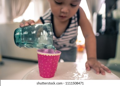 Cute Small Child Playing By Pouring Water From Glass To Another Glass On Small Table With Water Soak On Table, Learning Through Play