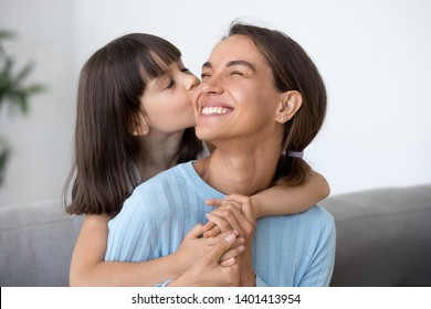 Cute small daughter kiss happy mom on cheek hugging her from behind, funny little caring preschooler kid piggyback embrace smiling mother showing love, child girl and mommy have sweet moment together