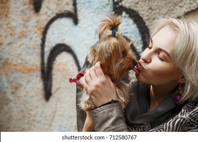 Cute Small Dog In The Arms Of A Beautiful Young Girl Licking Her Face Outdoors