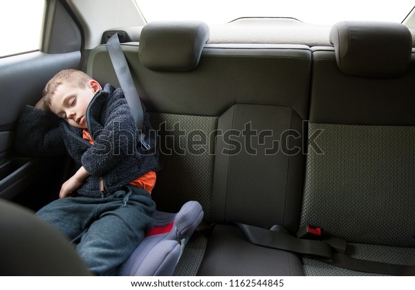 cute small forsaken child wearing warm\
jacket sleeping in inside car wearing seat\
belt