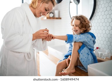 A cute small girl with mother in bathroom indoors at home, painting nails. - Powered by Shutterstock