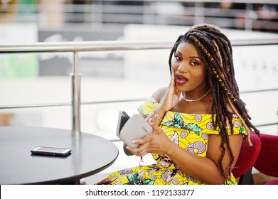 Cute Small Height African American Girl With Dreadlocks, Wear At Coloured Yellow Dress, Sitting On Cafe At Shopping Center And Looking At Her Wallet. No Money Concept.